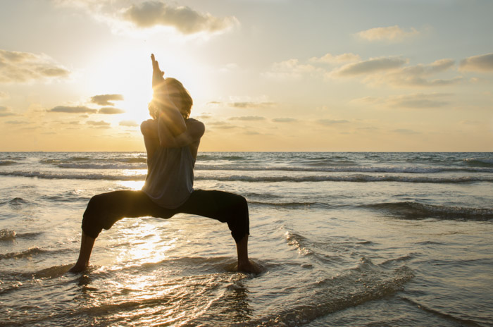 日落时分在海滩上做瑜伽的女人的剪影